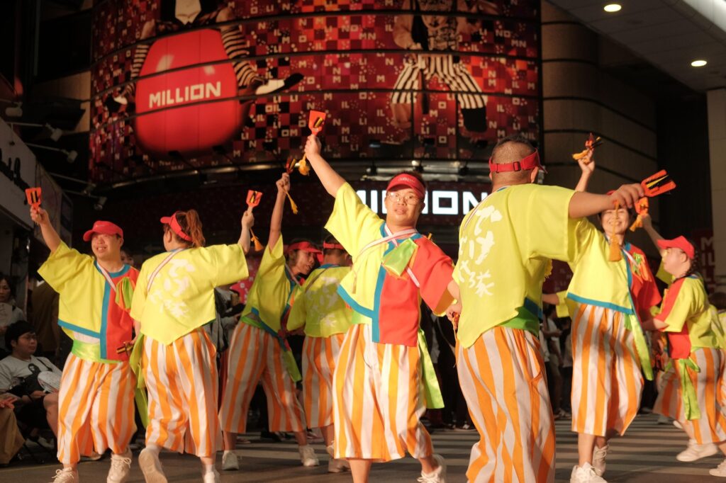 Arms lifted high and spinning around their partners, dancers in vibrant costumes fill the frame with movement and colour. Captured mid-performance at the Yosakoi Festival in Kochi Prefecture, Japan, this image radiates sheer, infectious joy.The Yosakoi Festival, held every summer, is a celebration of dance open to all, where teams including disabled performers take to the streets alongside others. In this photograph, there are no divisions, no qualifiers, only collective energy, rhythm, and pride. The scene invites us not just to observe but to join: to celebrate movement, connection, and the transformative power of dance.By centring disabled dancers within a mainstream cultural event, the image challenges assumptions about participation, embodiment, and belonging. It reminds us that spaces of joy and expression must be accessible to all, not as an exception, but as a vital part of community life.