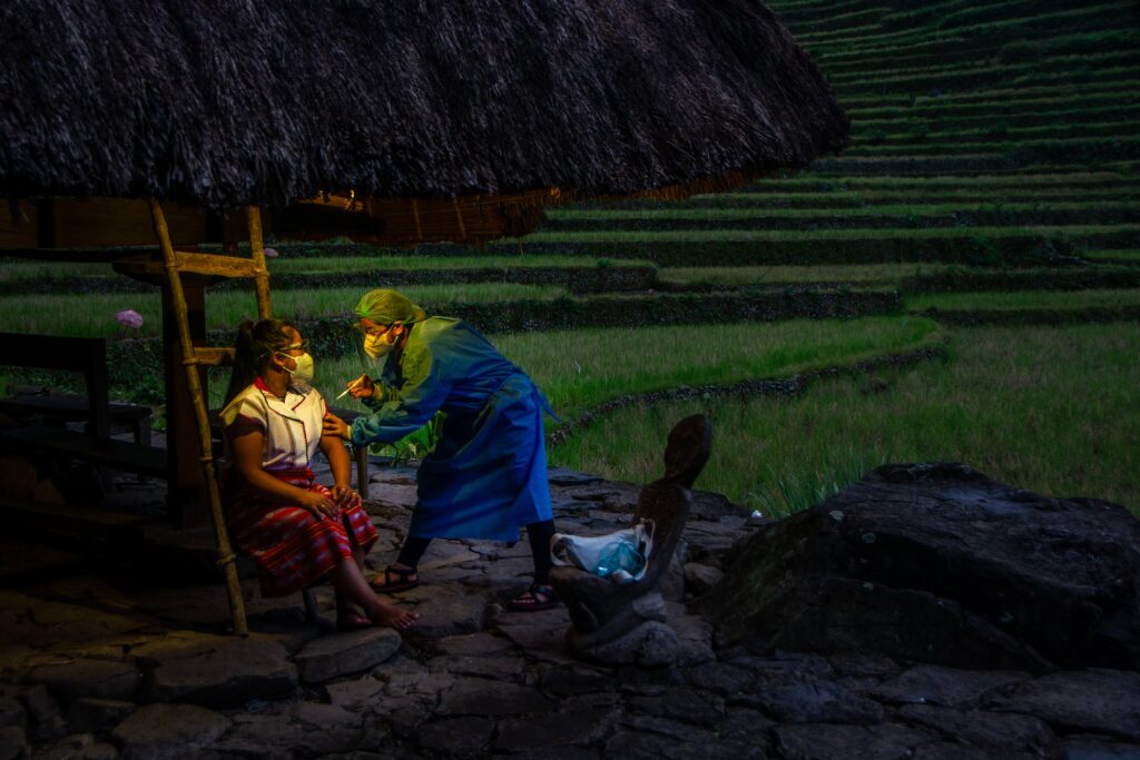 As dusk falls amid the steep slopes of the Banaue Rice Terraces, a woman receives care. Her masked face glowing with the quiet relief that help has come at last, reaching her through the gentle hands of a health worker.