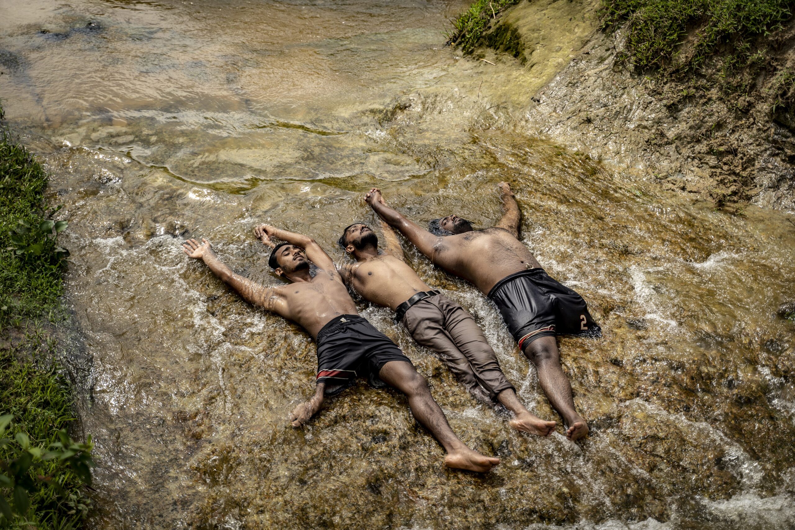 Three members of an amputee football club lie in the flowing waters of a river, arms raised and hands clasped above their heads.