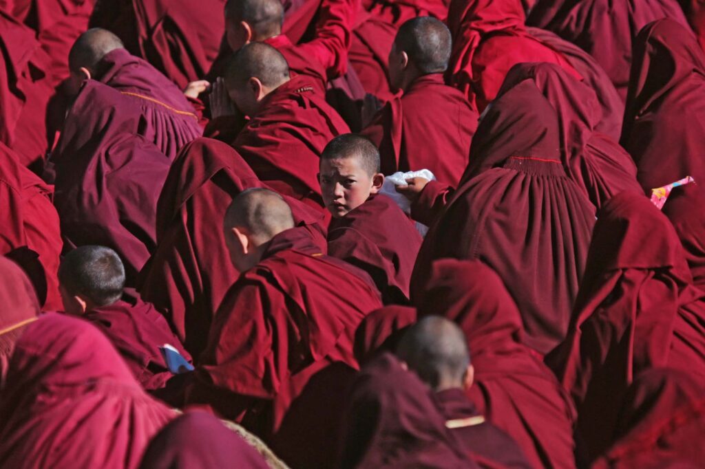 Among a sea of red robbed nuns, a young nun turns her head toward the camera during at Yarchen Gar, the world’s largest monastic settlement for Buddhist nuns.