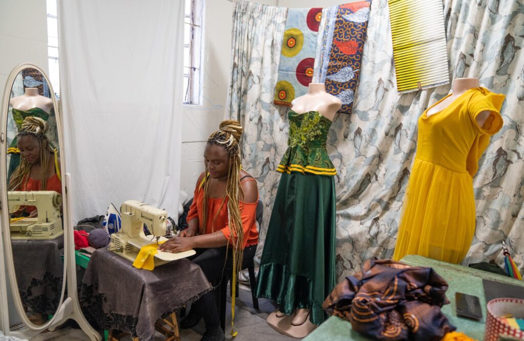 Leona Sibanda sews at her table in Johannesburg, surrounded by the colourful and intricate designs that fill her clothing store. She works steadily, cautiously.